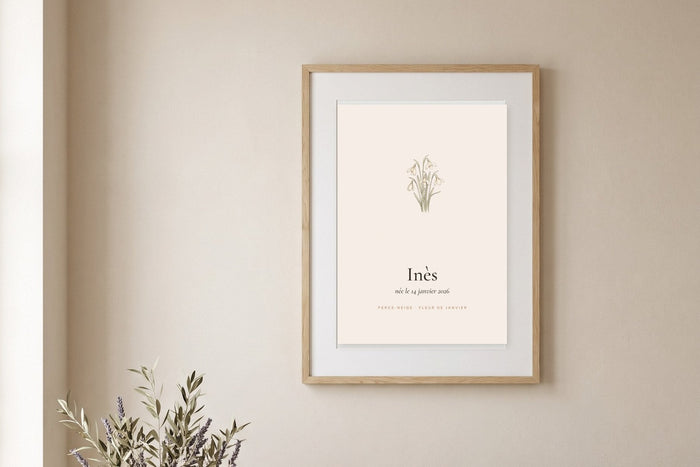 Affiche fleur de naissance avec une perce-neige à l'aquarelle et le prénom Inès, encadrée sur un mur beige