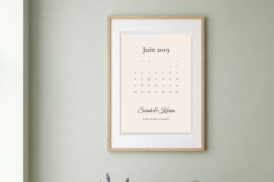 Affiche rencontre couple en calendrier avec le jour entouré et les prénoms Sarah et Karim, encadrée sur un mur vert sauge