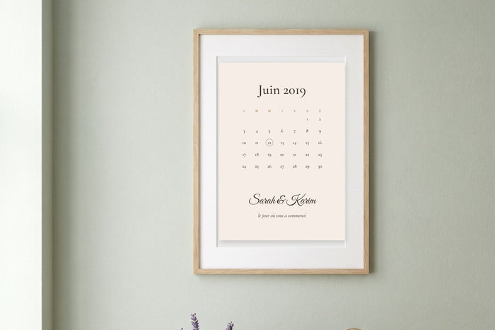 Affiche rencontre couple en calendrier avec le jour entouré et les prénoms Sarah et Karim, encadrée sur un mur vert sauge